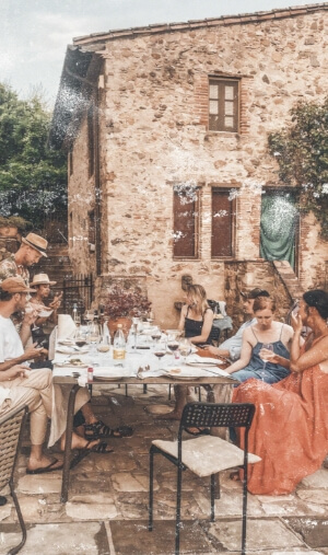 Carte postale vieillie avec des personnes atablées sur une terasse devant une maison en pierre