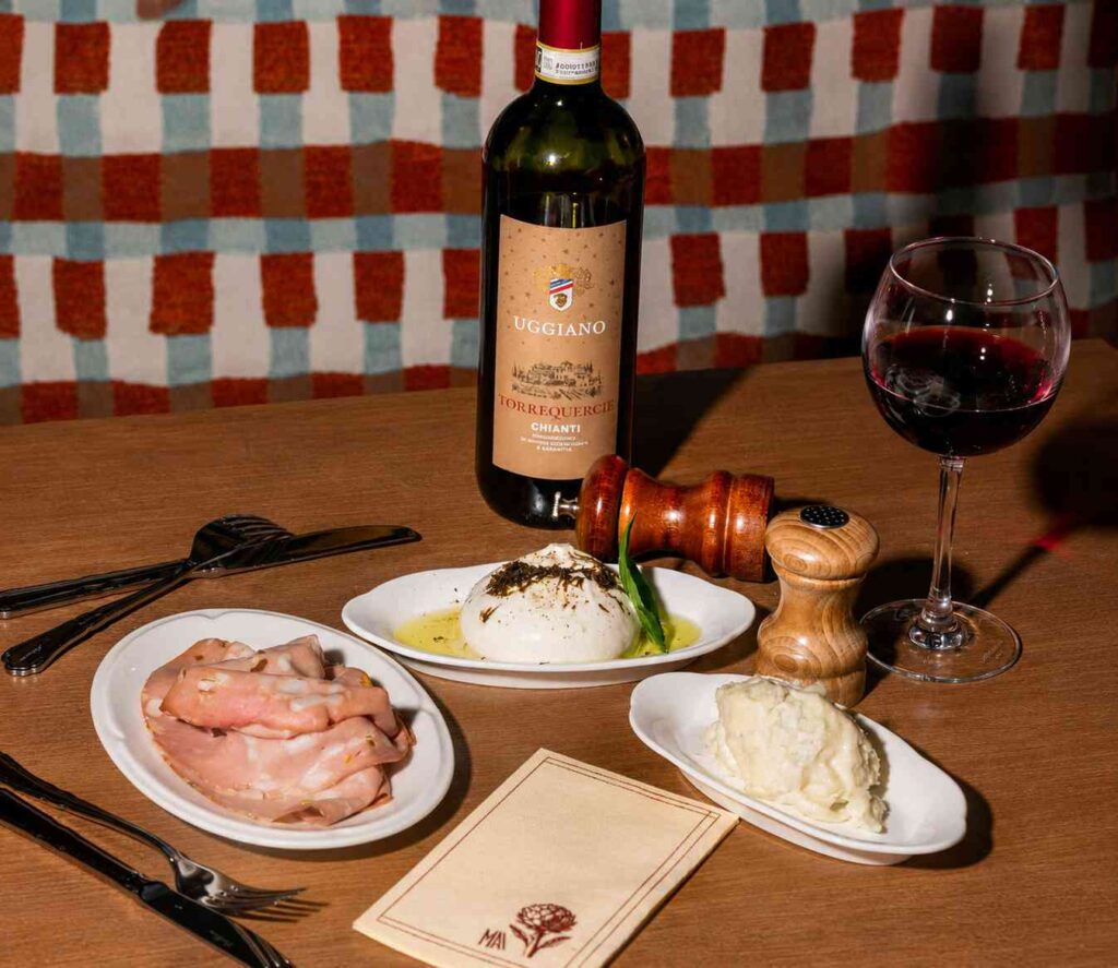 Bouteille de Chianti accompagnée de burrata, mortadelle et verre de vin rouge sur une table de restaurant italien.