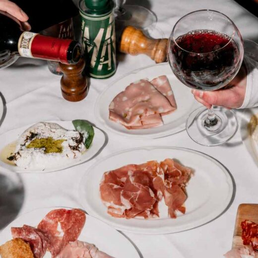 Table de restaurant italien garnie de charcuteries, burrata et verres de vin rouge pendant un repas convivial.