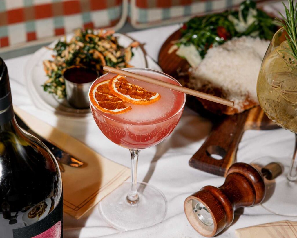 Cocktail signature servi dans une coupe avec agrumes séchés, présenté sur une table garnie de spécialités italiennes au Bouillon Caffè.