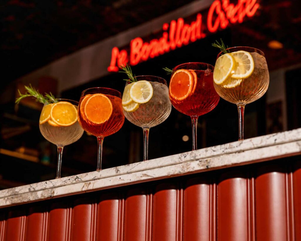 Sélection de cocktails italiens Sprtiz garnis d'agrumes et de romarin, présentés sur le comptoir du Bouillon Caffè dans une ambiance chaleureuse.