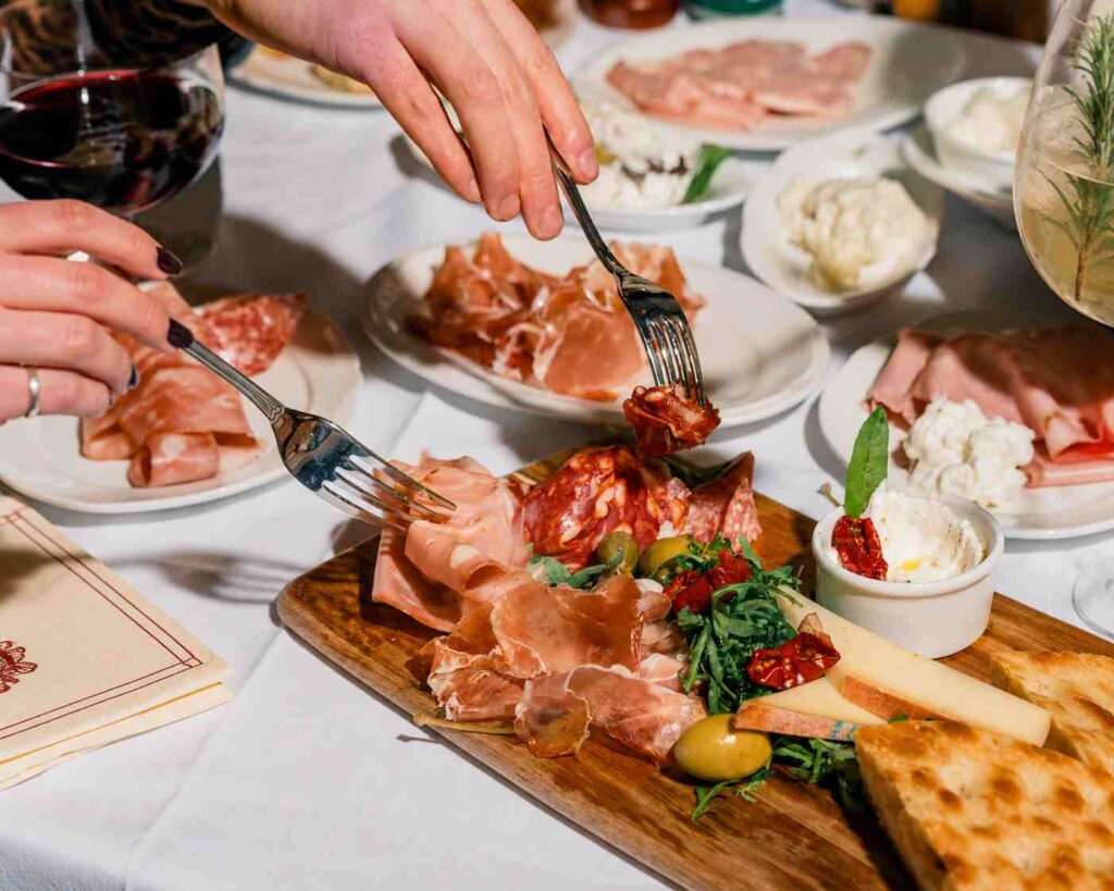 Planche d'antipasti italiens composée de charcuteries, fromages, olives et légumes grillés, partagée autour d'une table au Bouillon Caffè.
