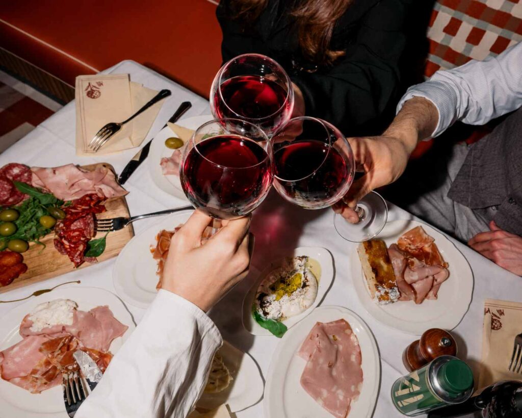 Trois personnes trinquent avec des verres de vin rouge autour d'une table garnie de spécialités italiennes au Bouillon Caffè.