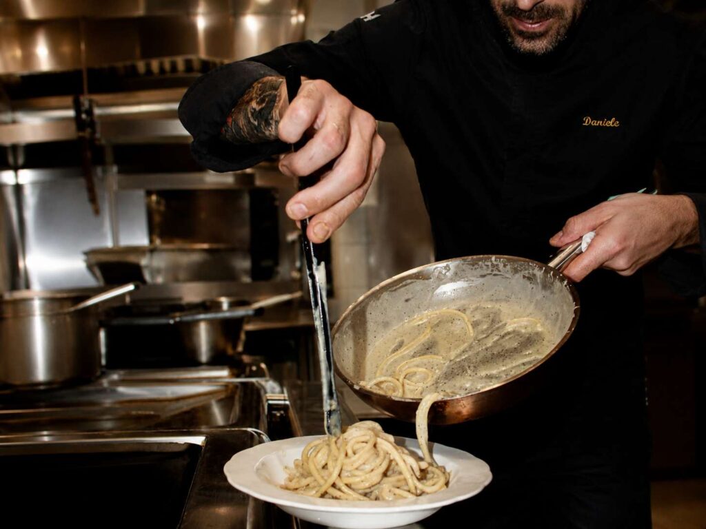 Chef dressant une assiette de spaghetti cacio e pepe dans la cuisine d’un restaurant italien.