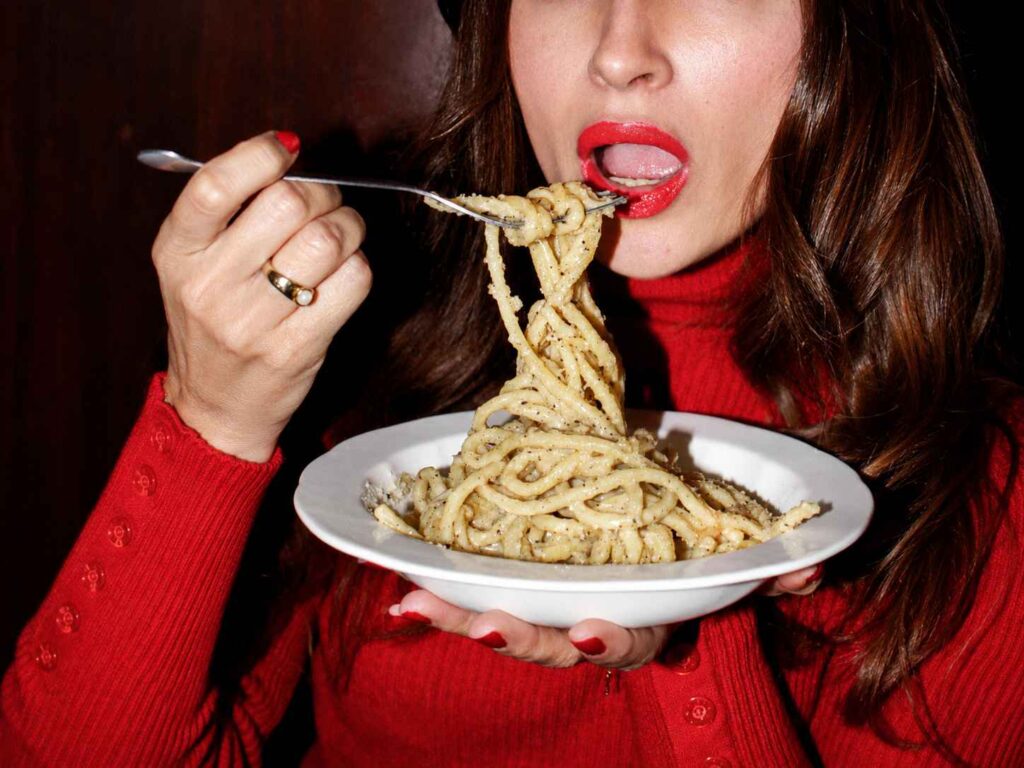 Cliente dégustant une fourchette de spaghetti cacio e pepe, assiette à la main, dans une ambiance chaleureuse de restaurant italien