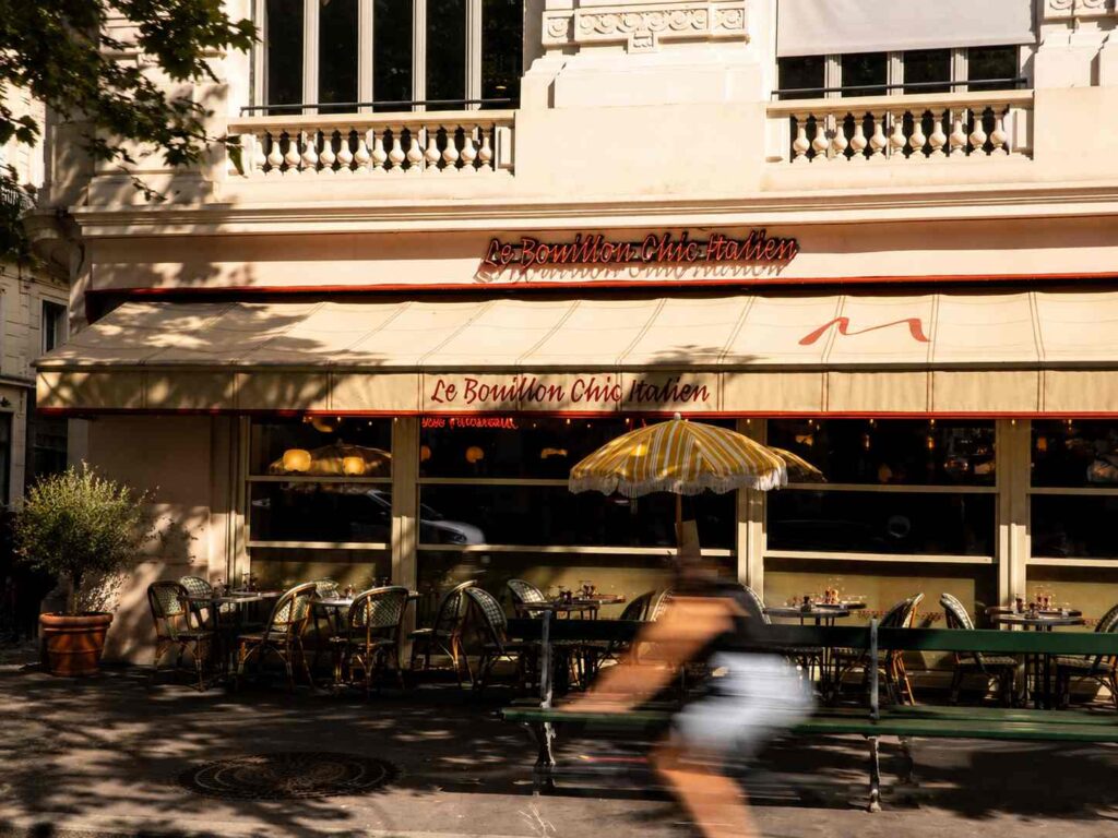 Façade de Ma Bouillon Chic Italien avec sa terrasse ensoleillée, ses tables en extérieur et un cycliste passant devant le restaurant