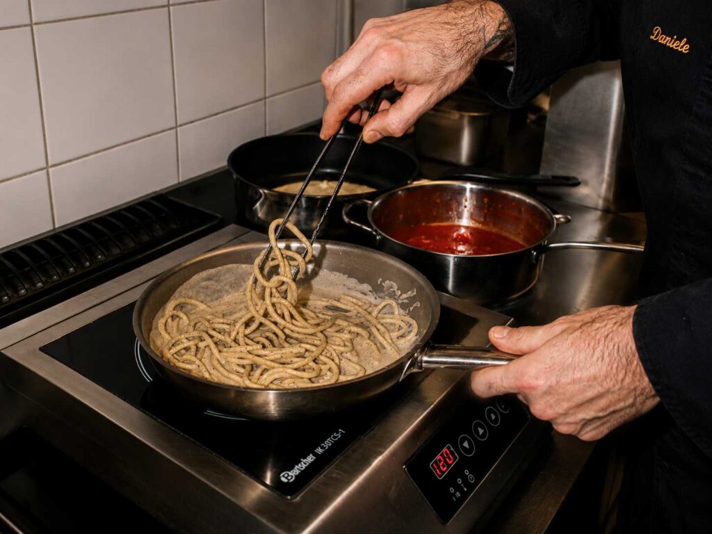 Préparation de spaghetti cacio e pepe dans une poêle par un chef en cuisine, juste avant le dressage de l’assiette.