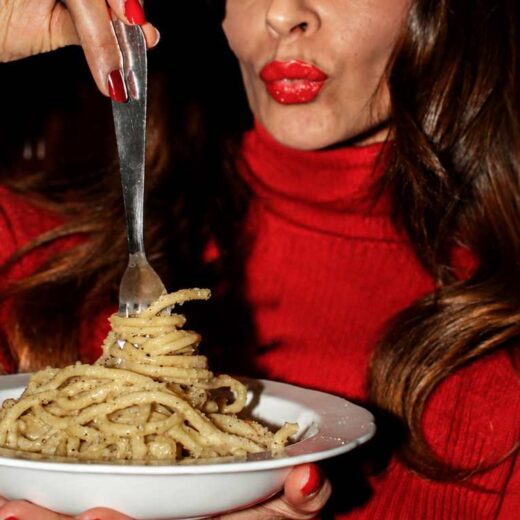 Close-up of a plate of spaghetti cacio e pepe held by a customer in the cozy atmosphere of an Italian restaurant