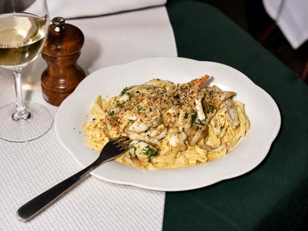 Assiette de tagliatelles en sauce crémeuse garnies de chair de crabe, accompagnée d'un verre de vin blanc sur une table de restaurant italien